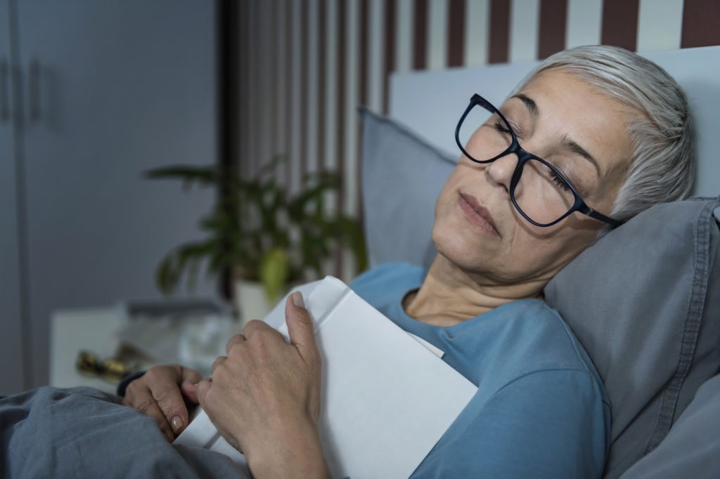 sleep senior woman falling asleep with a glasses on and a book on her chest - Channel Islands Family Dental Office | Dentist In Ventura County