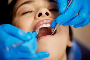Dentista realiza procedimiento a mujer. Mujer recibe tratamiento dental. ¿Por Qué Los Chequeos Dentales Son Esenciales?