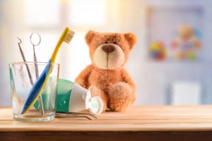 glass cup and teddy on wooden table in room with toys background.
