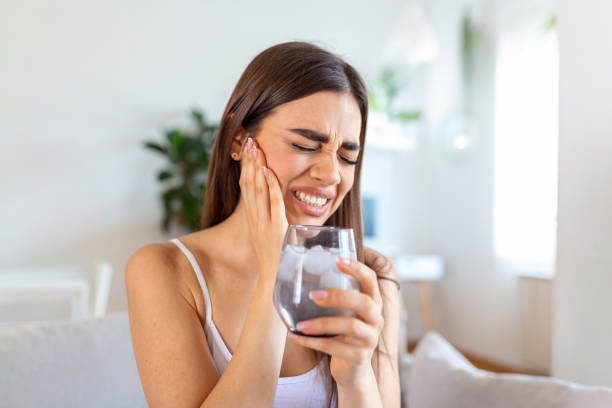 Young woman with sensitive teeth and hand holding glass of cold water with ice. Healthcare concept.