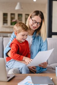 Vertical portrait of a small toddler kid child son helping her busy young mother with freelance